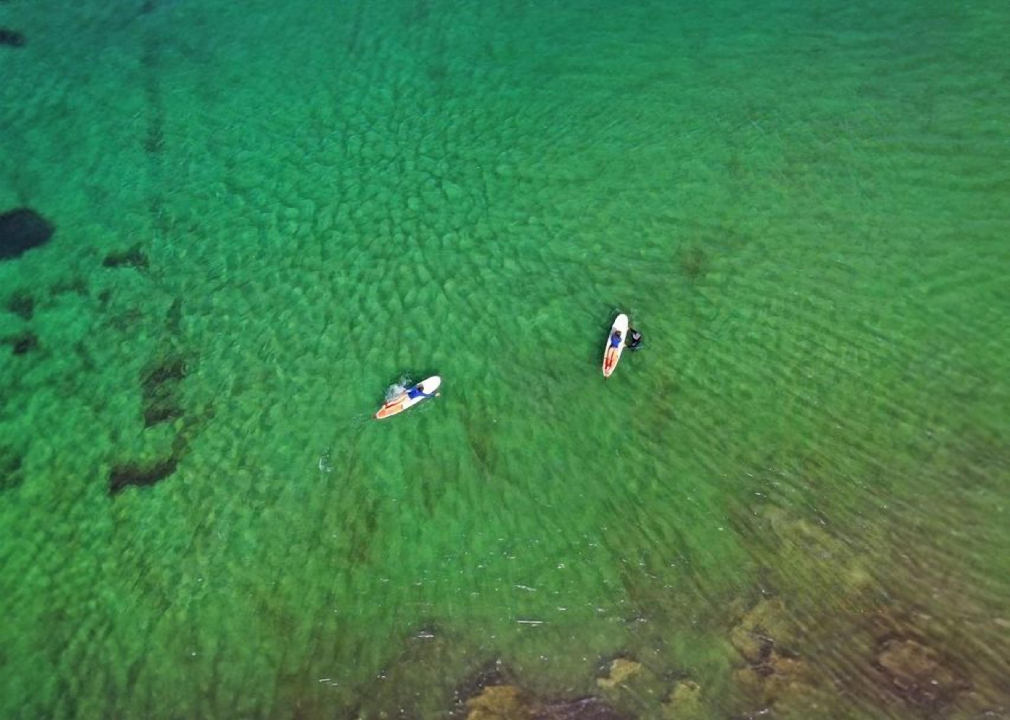 An aerial view of a beach with two surfboards floating on the water.