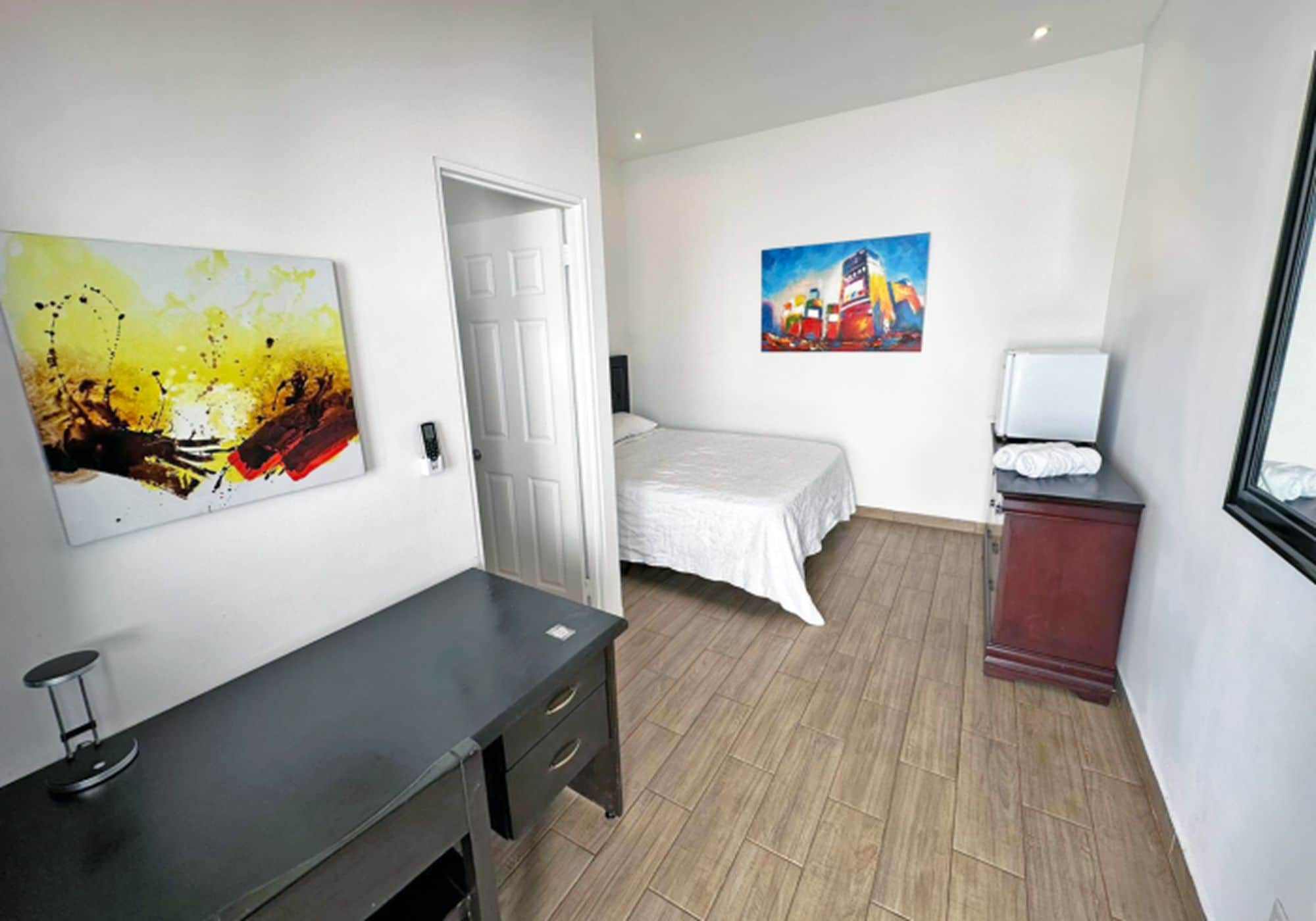 Una habitación de hotel con una cama, un escritorio, una silla y dos cuadros en la pared.