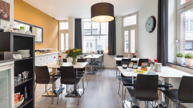 A modern dining area with a central table, chairs, and a hanging light fixture. - B&b De Hofnar Roermond (Roermond)
