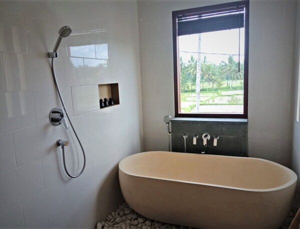 A modern bathroom with a freestanding bathtub, a showerhead, and a window with a view of greenery. -  DLobong Suites Ubud (Ubud)
