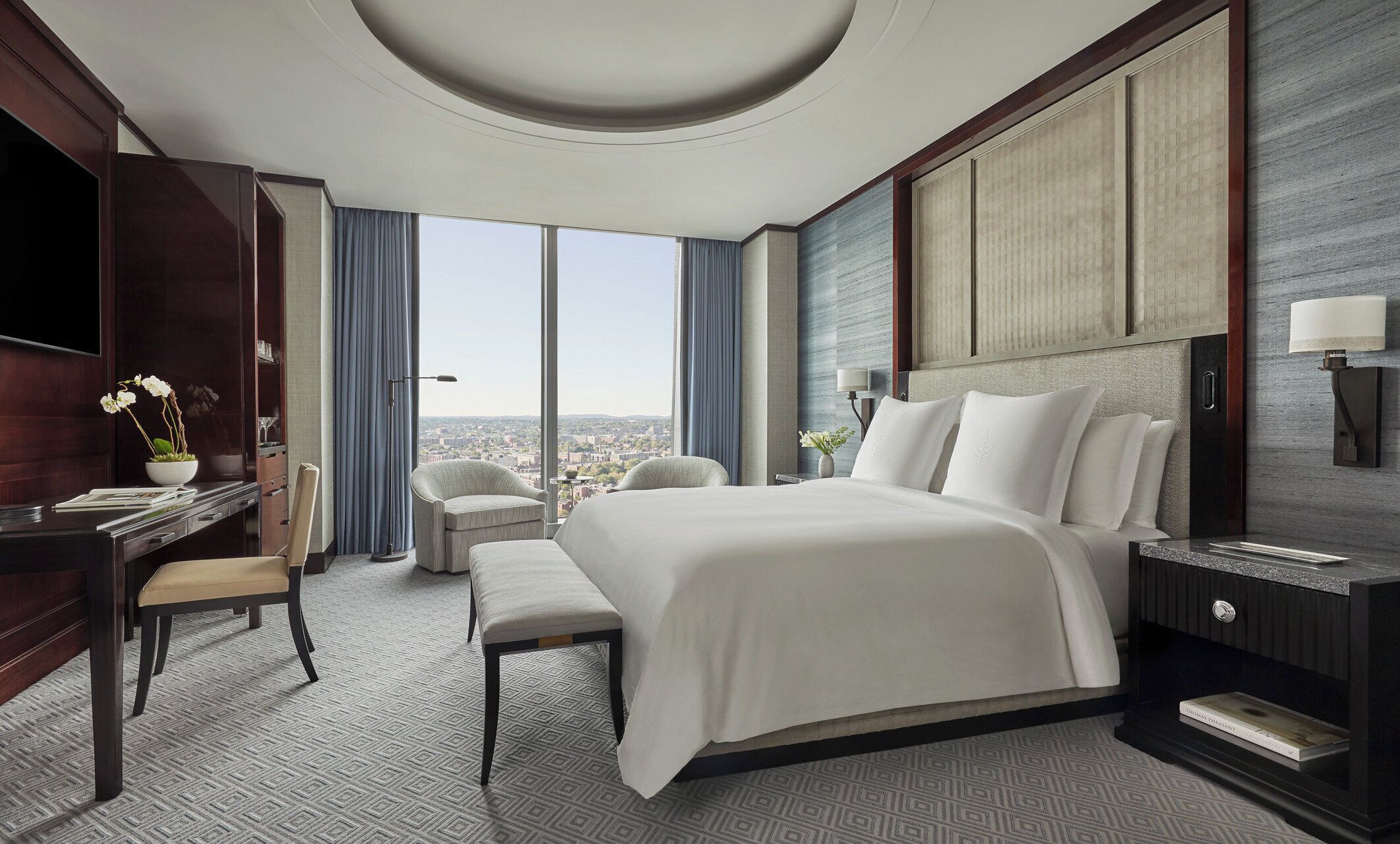 A modern hotel room with a large bed, a desk, a chair, and a view of the city.
