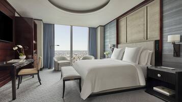 A modern hotel room with a large bed, a desk, a chair, and a view of the city.