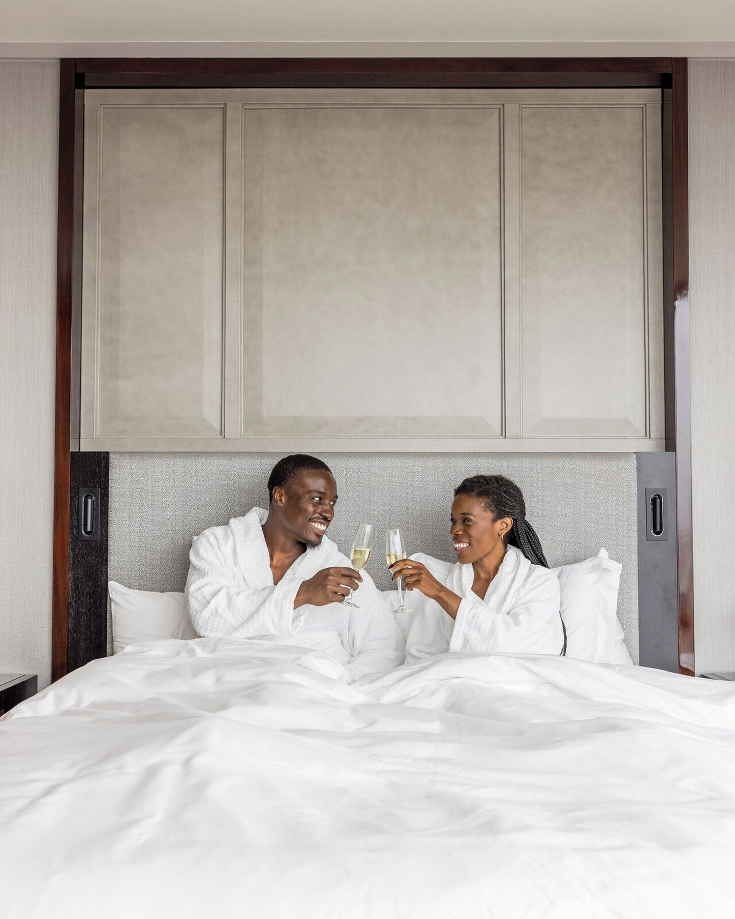 A hotel room with a large bed, a wooden headboard, and a grey textured wall.