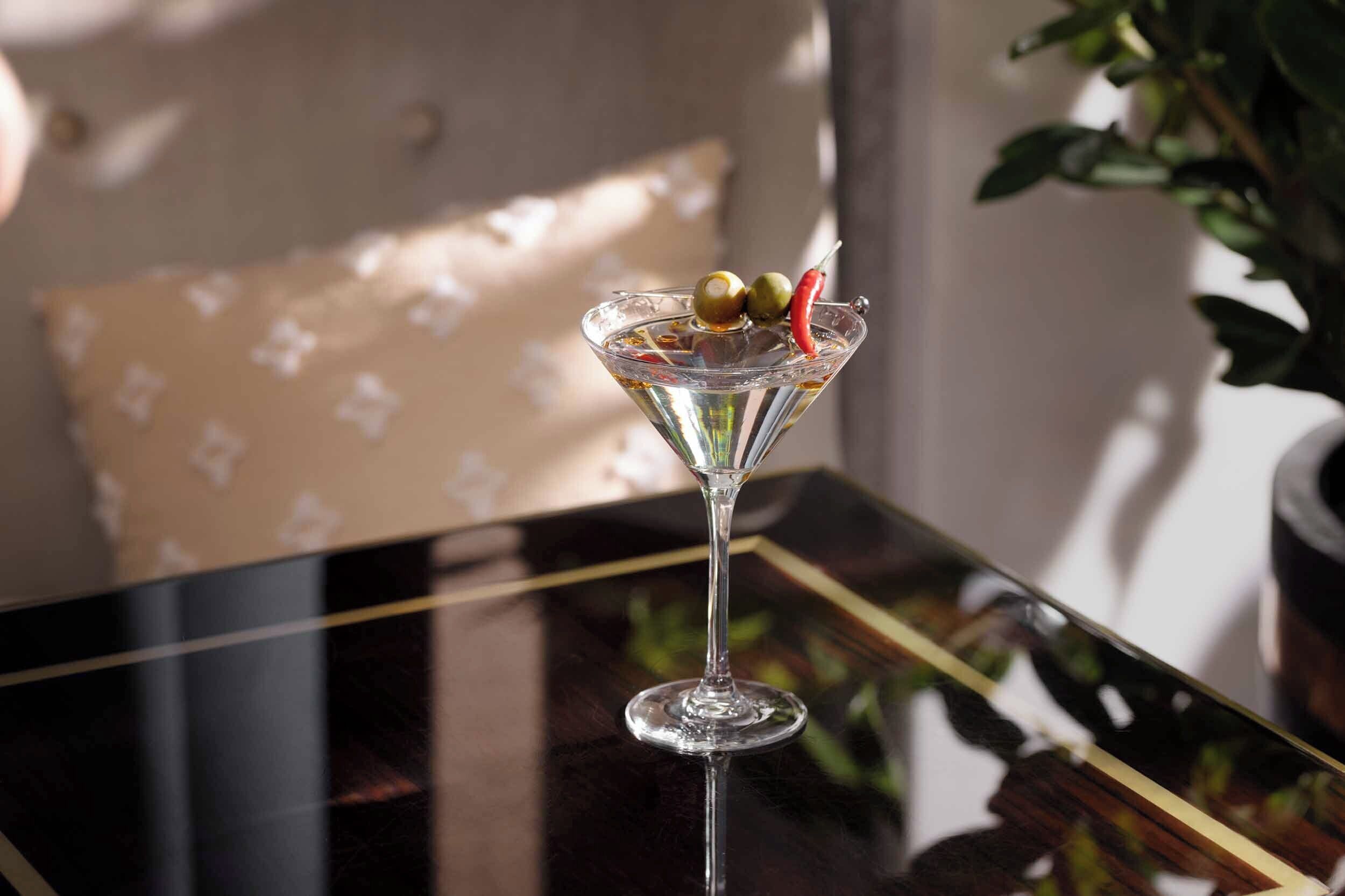 Un verre à martini posé sur une surface réfléchissante, avec une plante en arrière-plan.