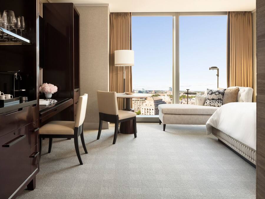 Habitación de hotel con cama, escritorio, silla, televisor y vista a la ciudad.