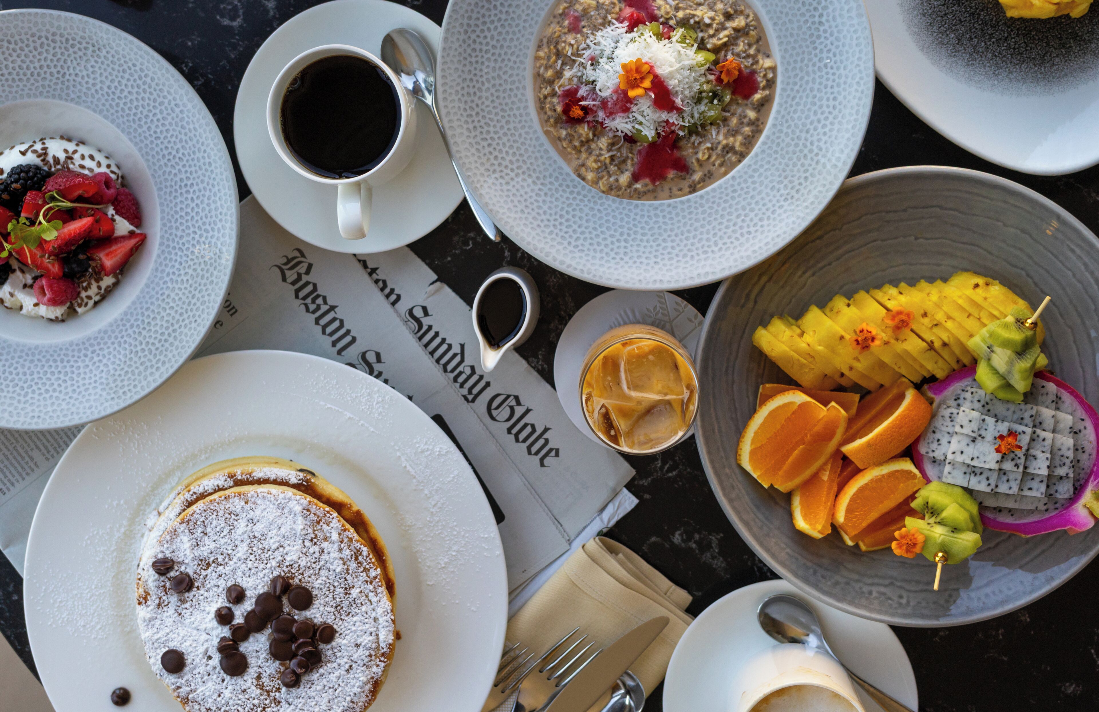Une table avec différents plats, une tasse de café et un journal.