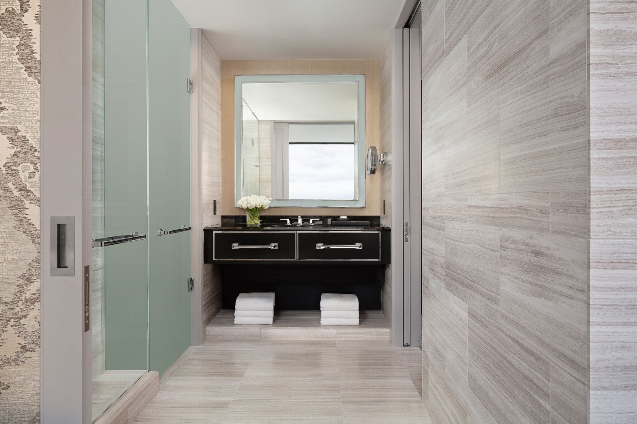 A modern bathroom with a glass shower enclosure, a black vanity with two drawers, and a large mirror above the sink.