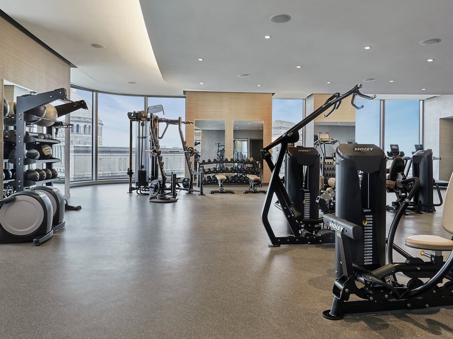 A modern gym with various exercise equipment, large windows, and a clean, spacious layout.