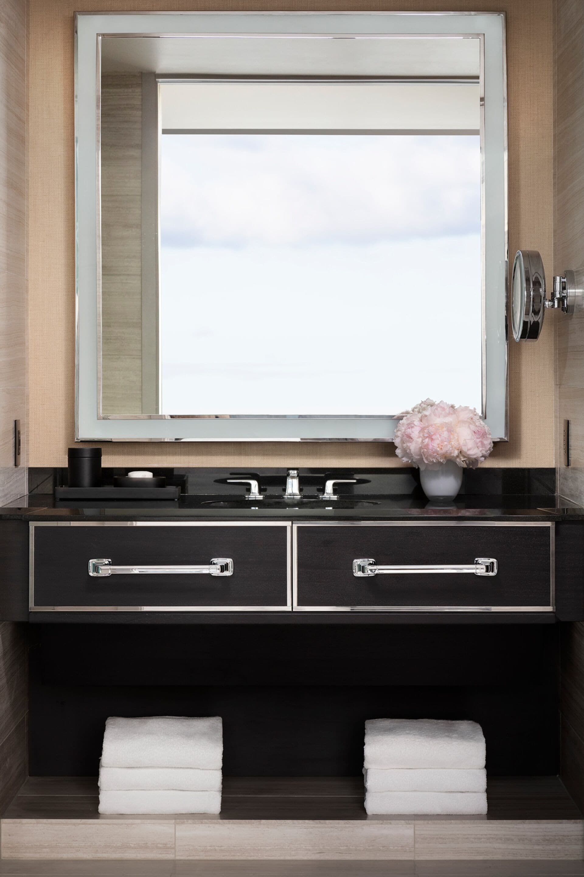 A bathroom with a large mirror, a black vanity, two towels, and a vase with flowers.