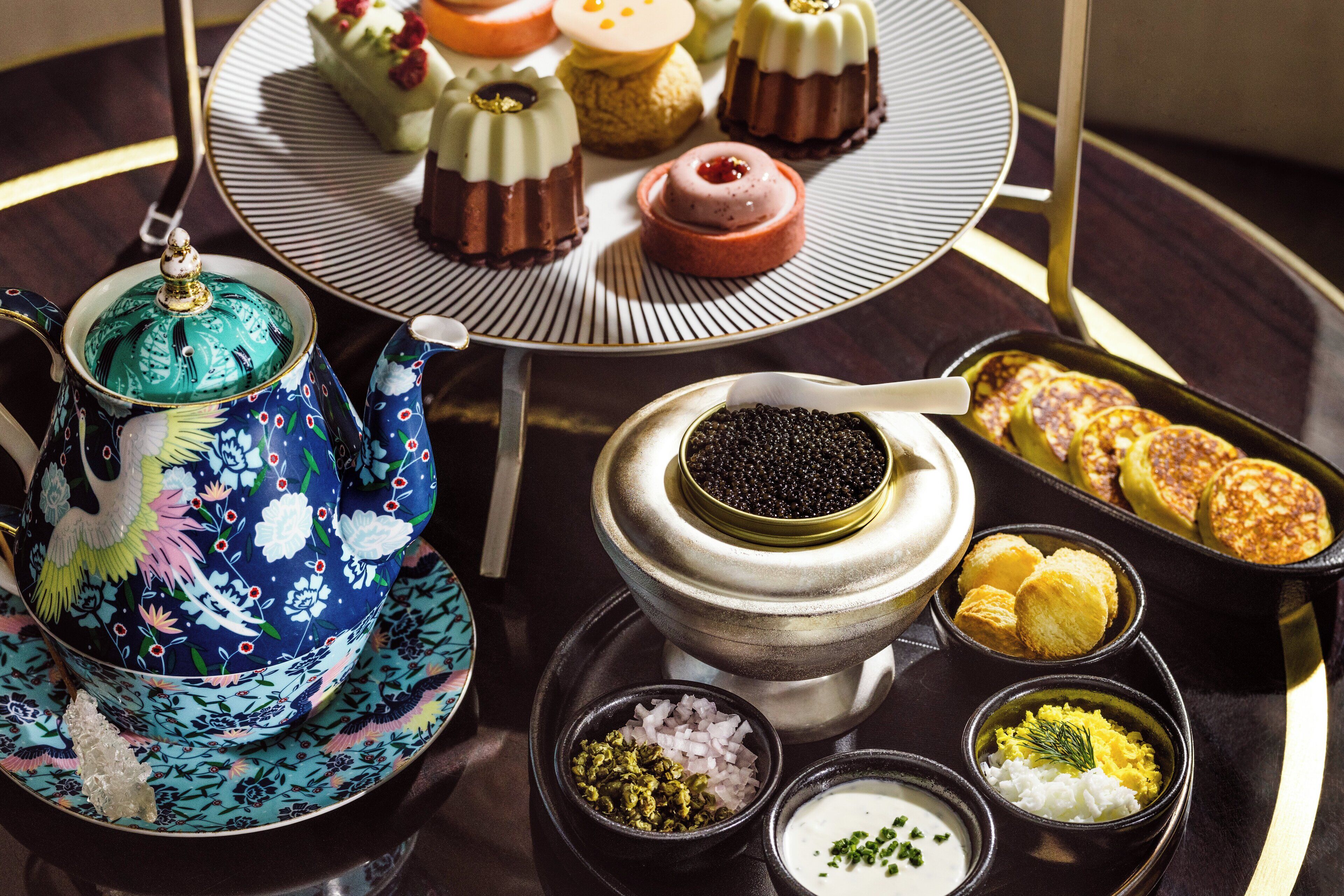 Un juego de té con tetera y tazas, un cuenco de caviar negro y diferentes platos pequeños con comida.