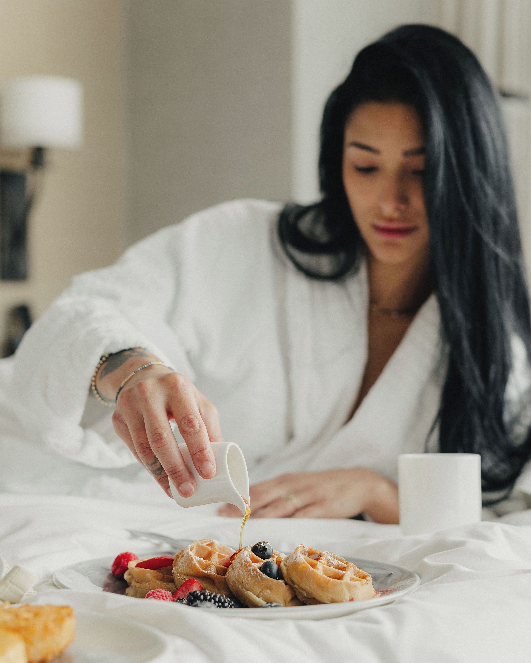 A person in a white robe pouring syrup onto waffles with berries.