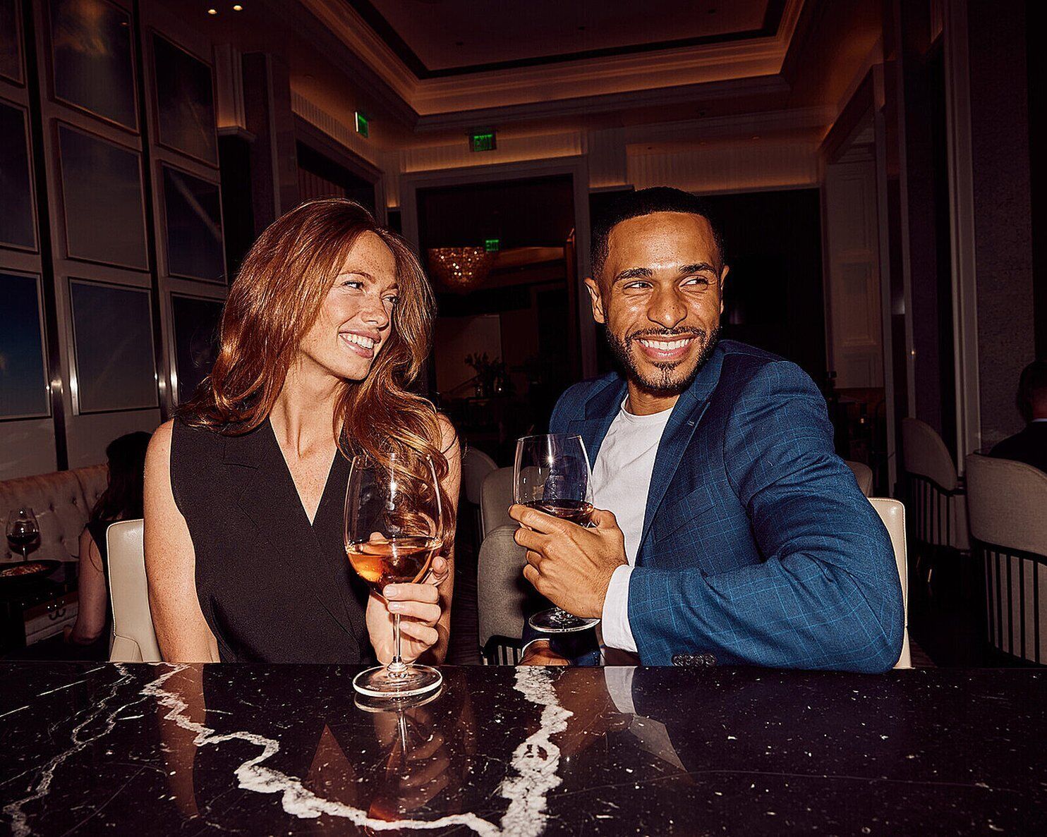 Two people seated at a table with a marble surface, holding drinks.