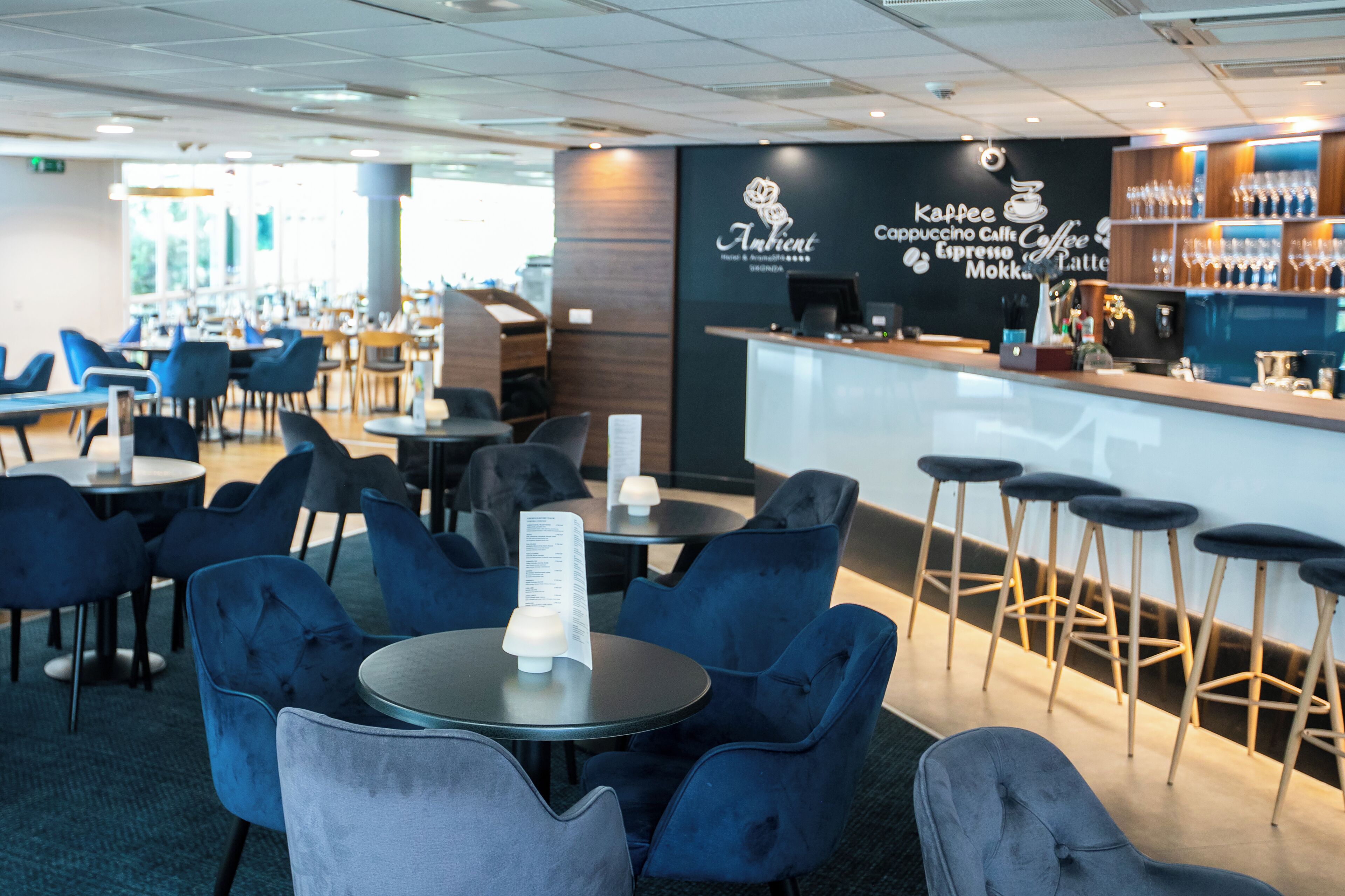 A modern cafe with blue upholstered chairs, a bar area with stools, and a menu stand.