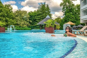 A swimming pool with a person in the water, surrounded by trees and a gazebo. - Ambient Hotel & Aromaspa Sikonda (Komlo)