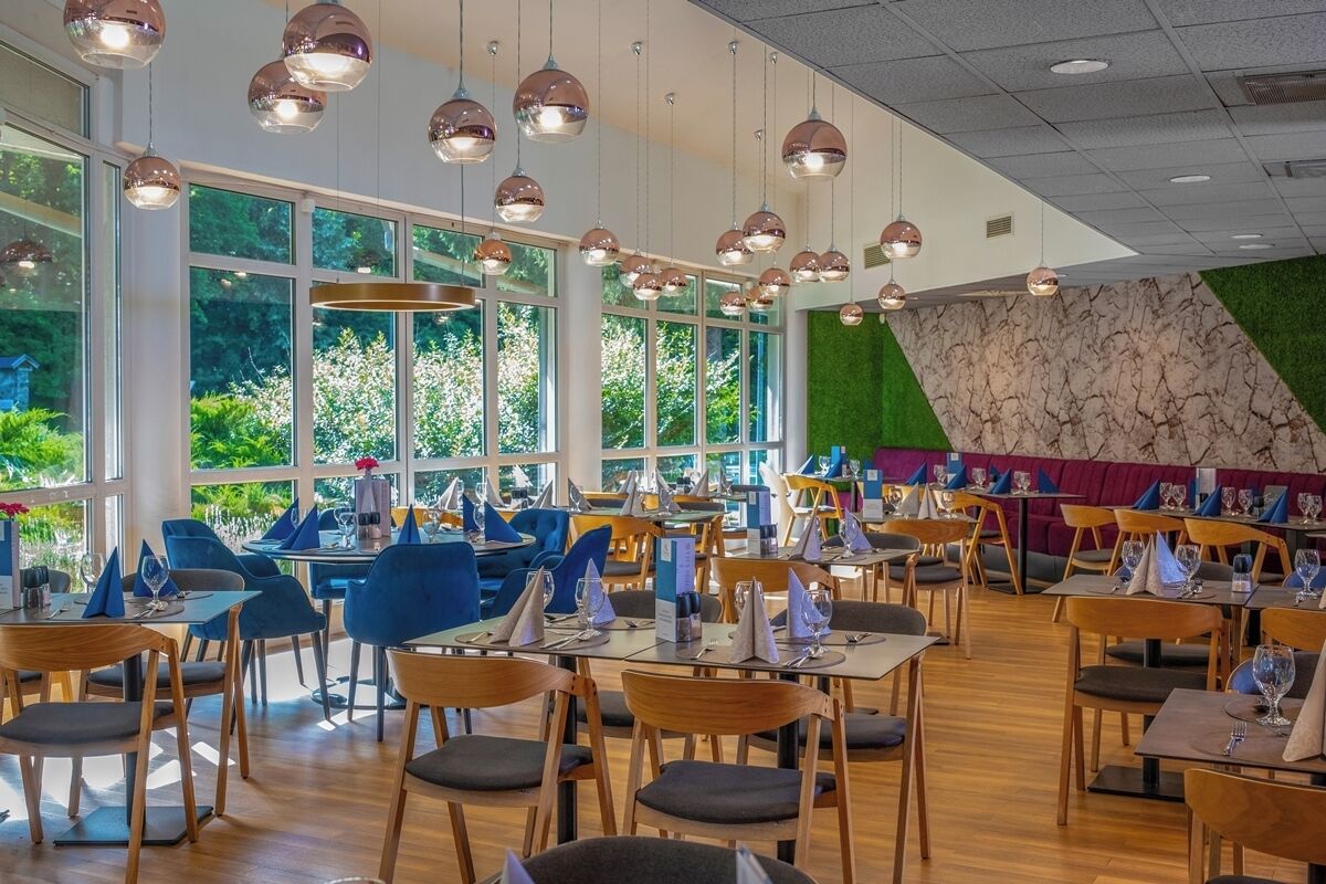 A modern restaurant with round tables and chairs, large windows, and hanging spherical lights.