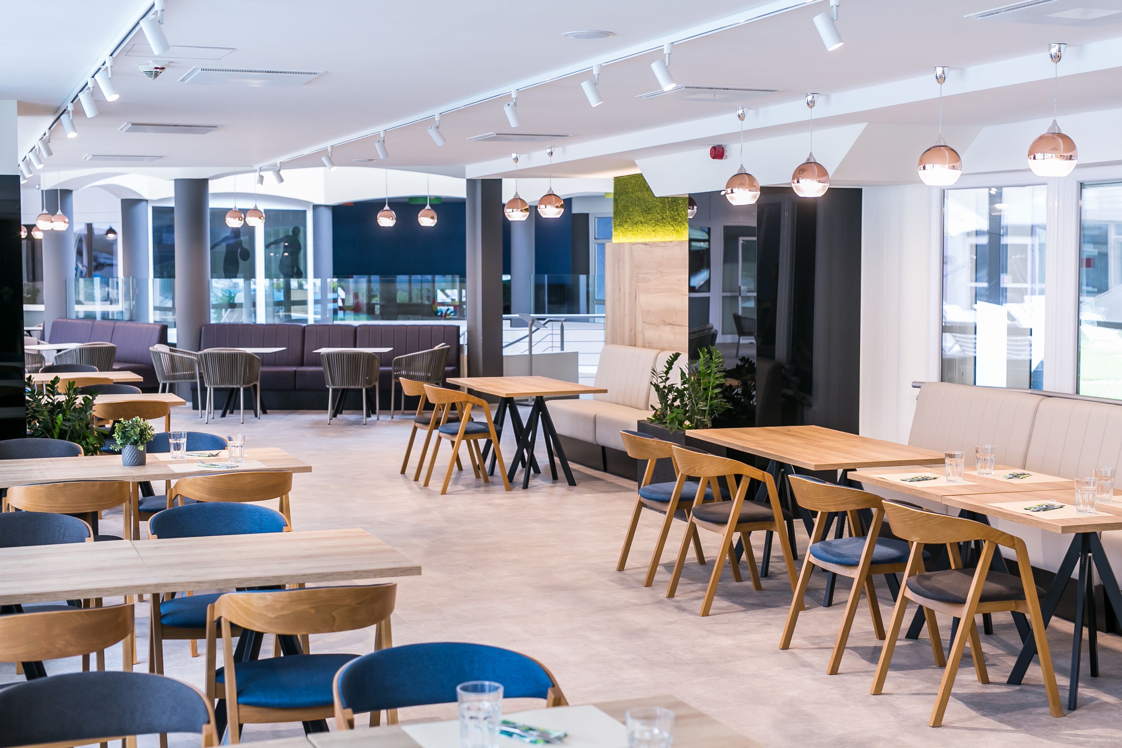 A modern restaurant interior with wooden tables and chairs, large windows, and pendant lighting.
