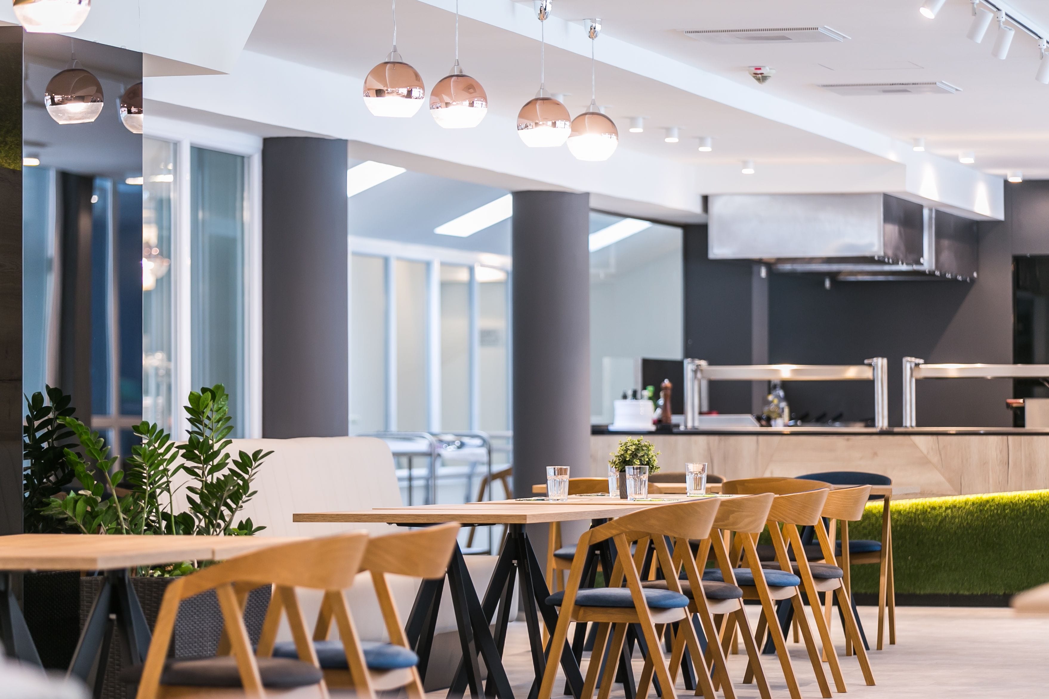 Un espace de restauration moderne avec des tables et des chaises en bois, des plantes en pot et des luminaires suspendus.