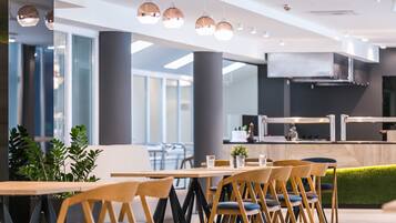 Un espace de restauration moderne avec des tables et des chaises en bois, des plantes en pot et des luminaires suspendus.