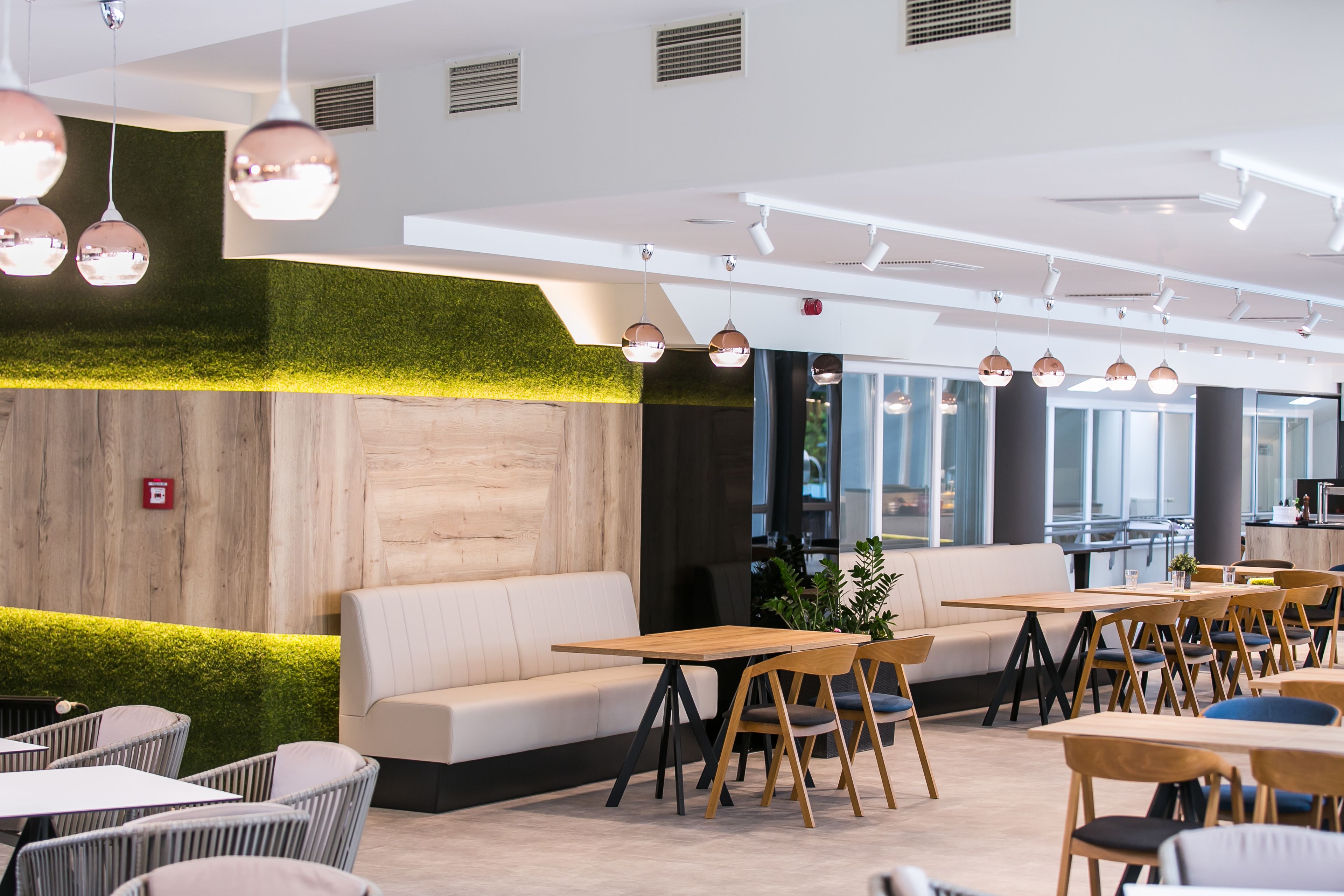 A modern indoor space with a green wall, wooden tables, and a white sofa.