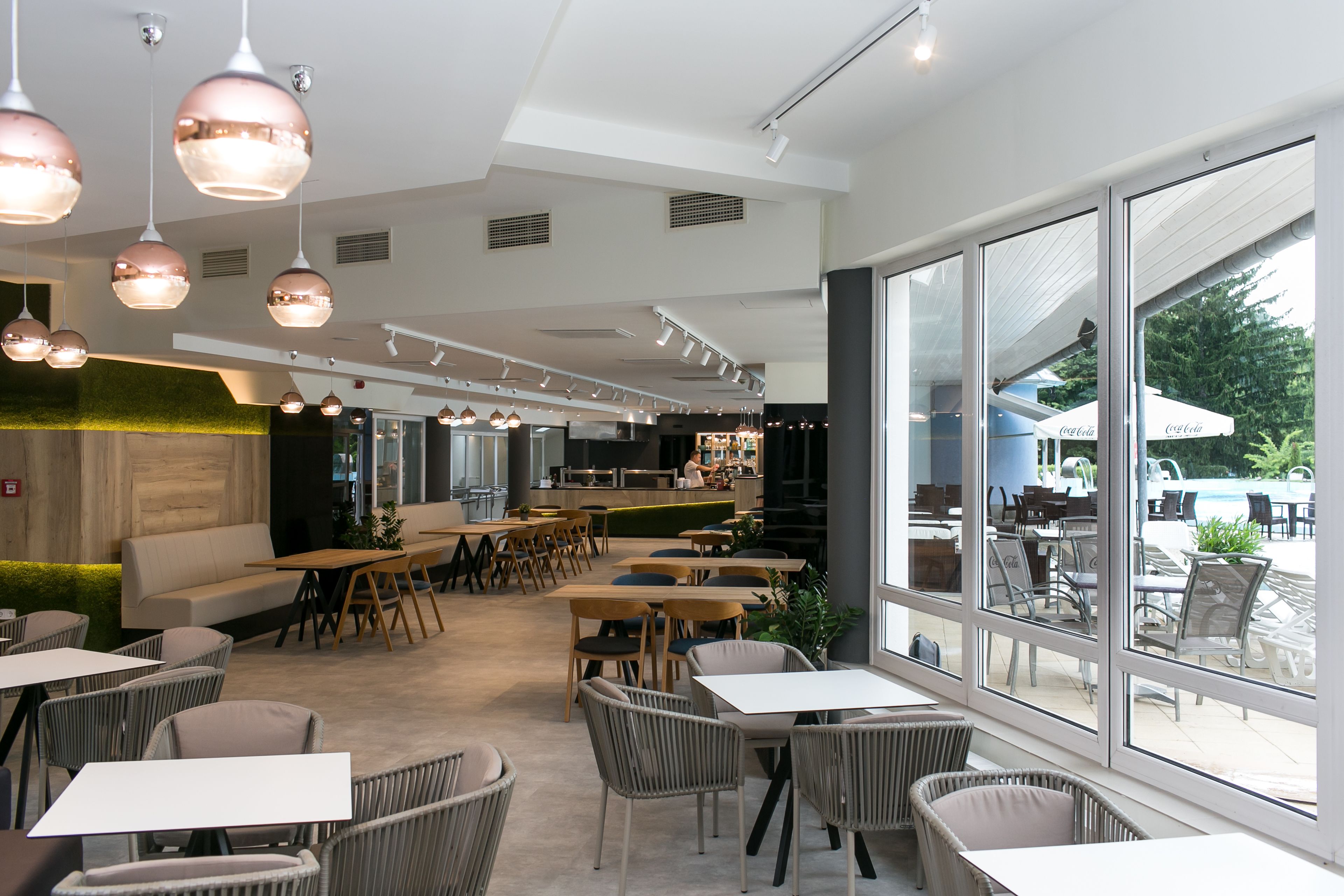 Un comedor moderno con mesas y sillas, ventanas amplias y una zona de mostrador.