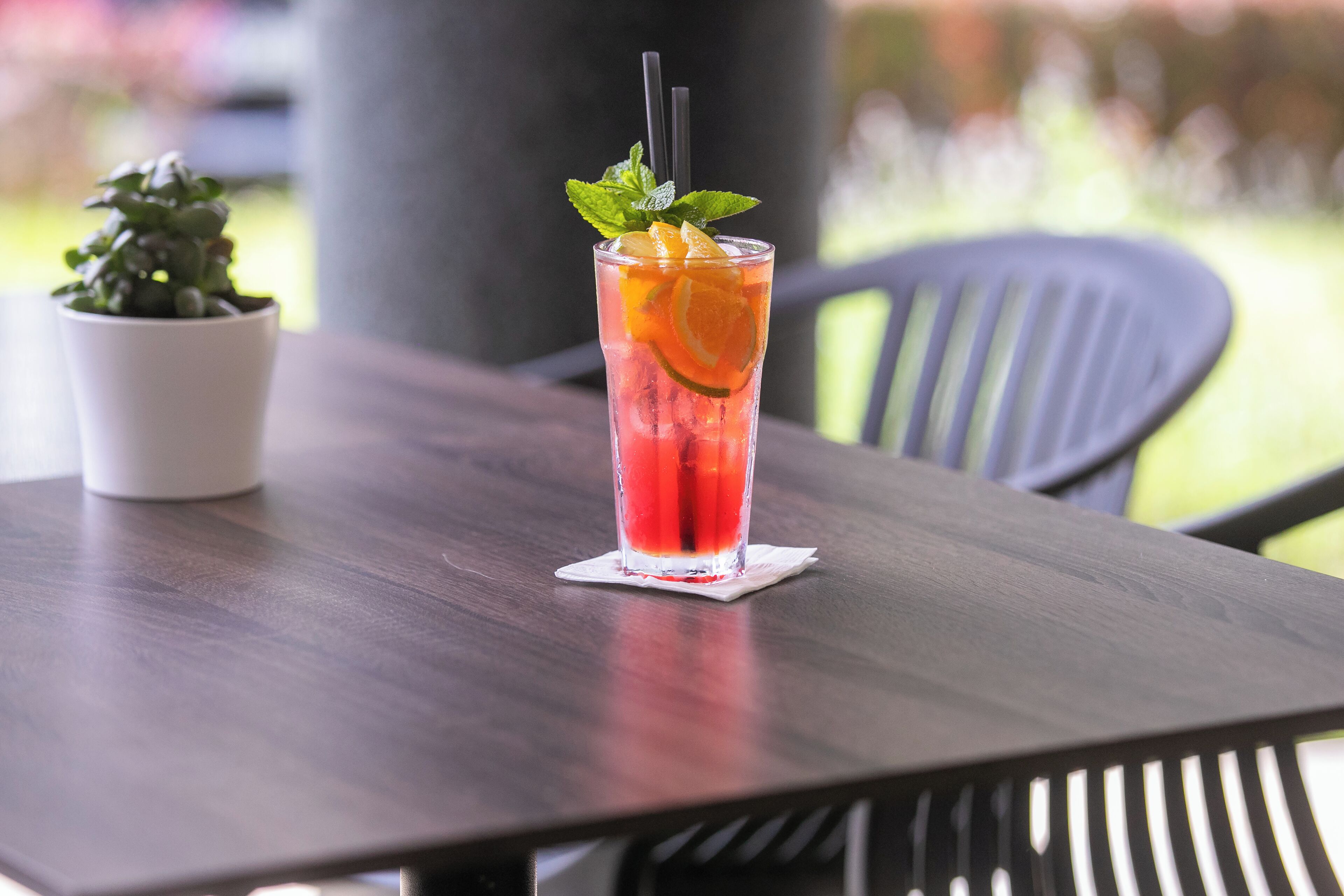 A glass of red beverage with a straw and mint garnish on a wooden table.