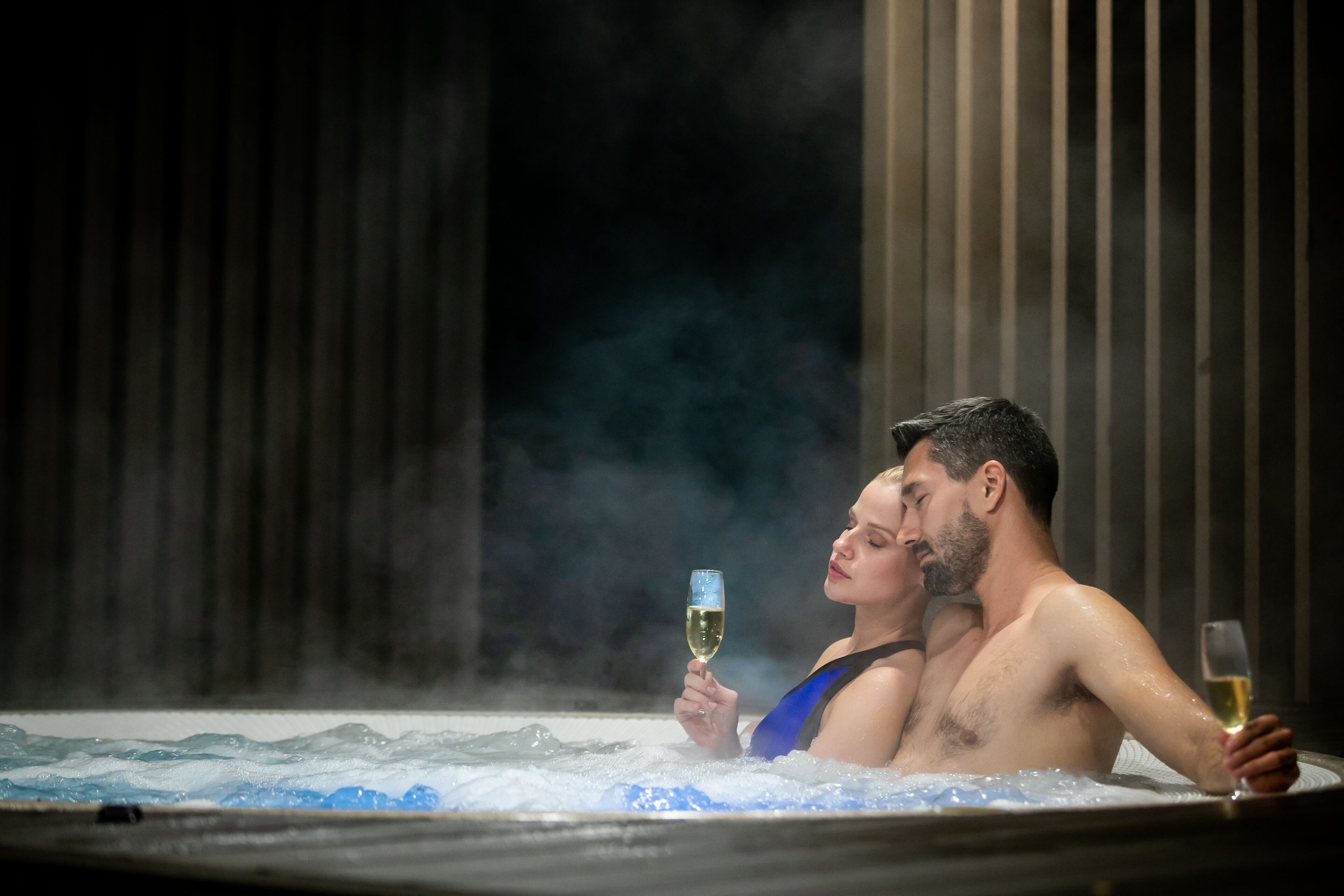 A couple in a hot tub with steam, holding glasses of champagne.