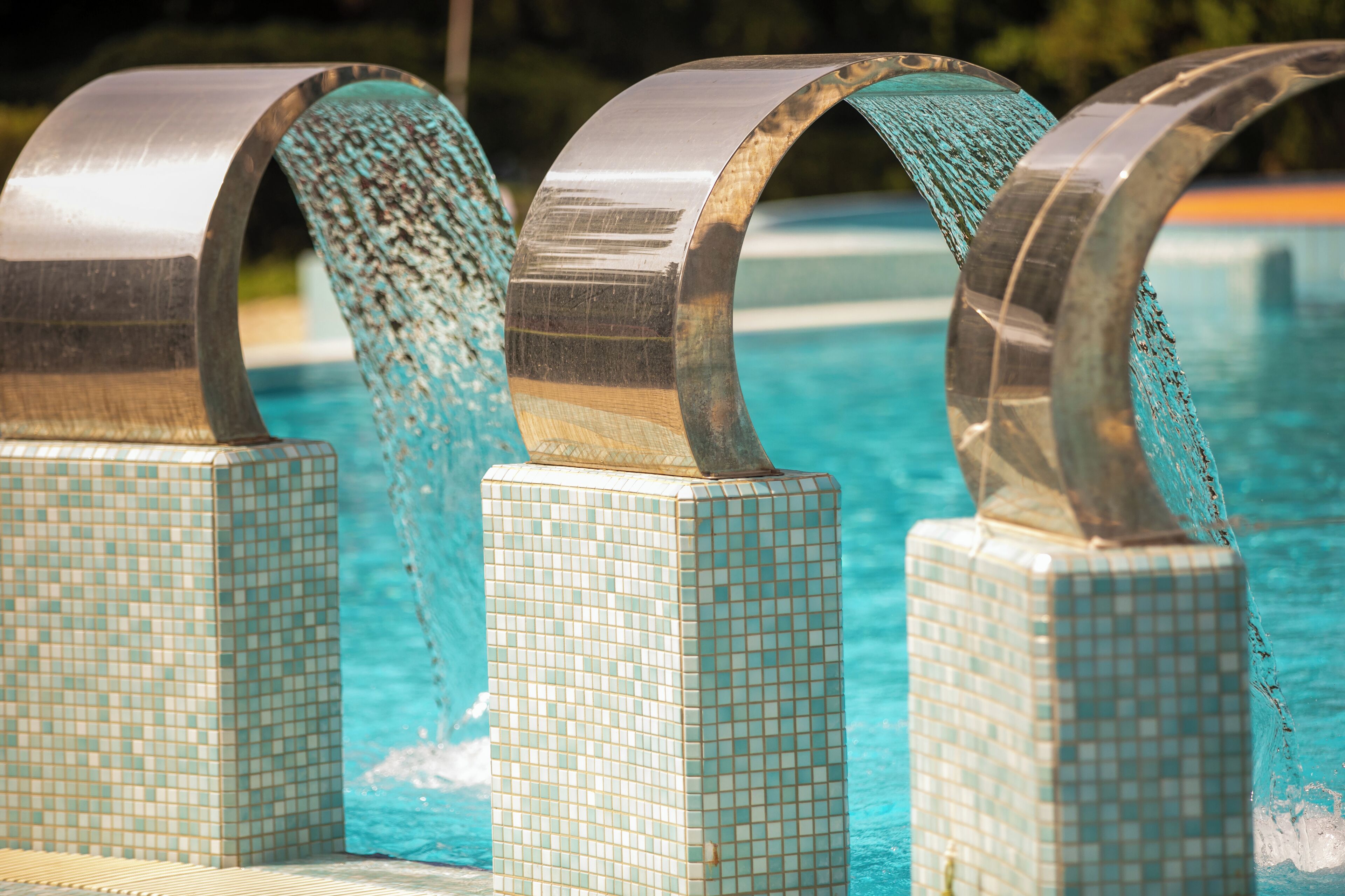 Una piscina con tre strutture metalliche curve e gradini piastrellati.