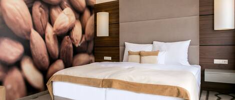 A modern hotel room with a large bed, a headboard with a wooden panel, and a wall mural of almonds.