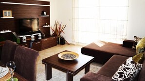 A modern living room with a flat-screen TV, dark wood shelving, a brown sofa, and a coffee table.