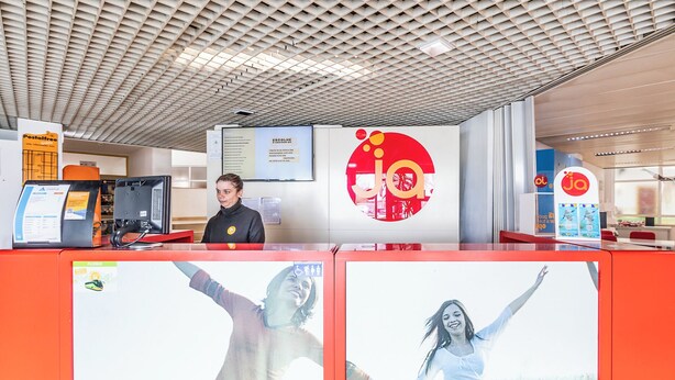 Een modern ontworpen receptiebalie, een digitaal scherm en een logo op de muur.