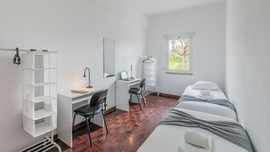 Een kamer met een bureau, stoel, bed en een raam met uitzicht op bomen.