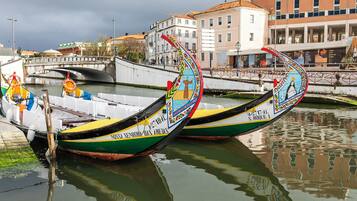 Two traditional boats docked at a waterfront, with buildings and a bridge in the background.