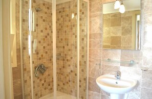 A bathroom with a glass shower enclosure, a sink, and a mirror.