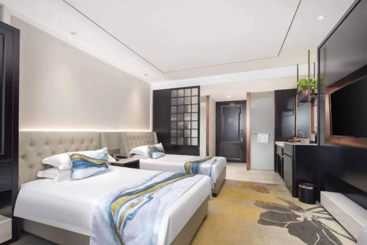 Een hotelkamer met twee bedden, een televisie, een bureau en een zichtbare badkamer door een geopende deur.