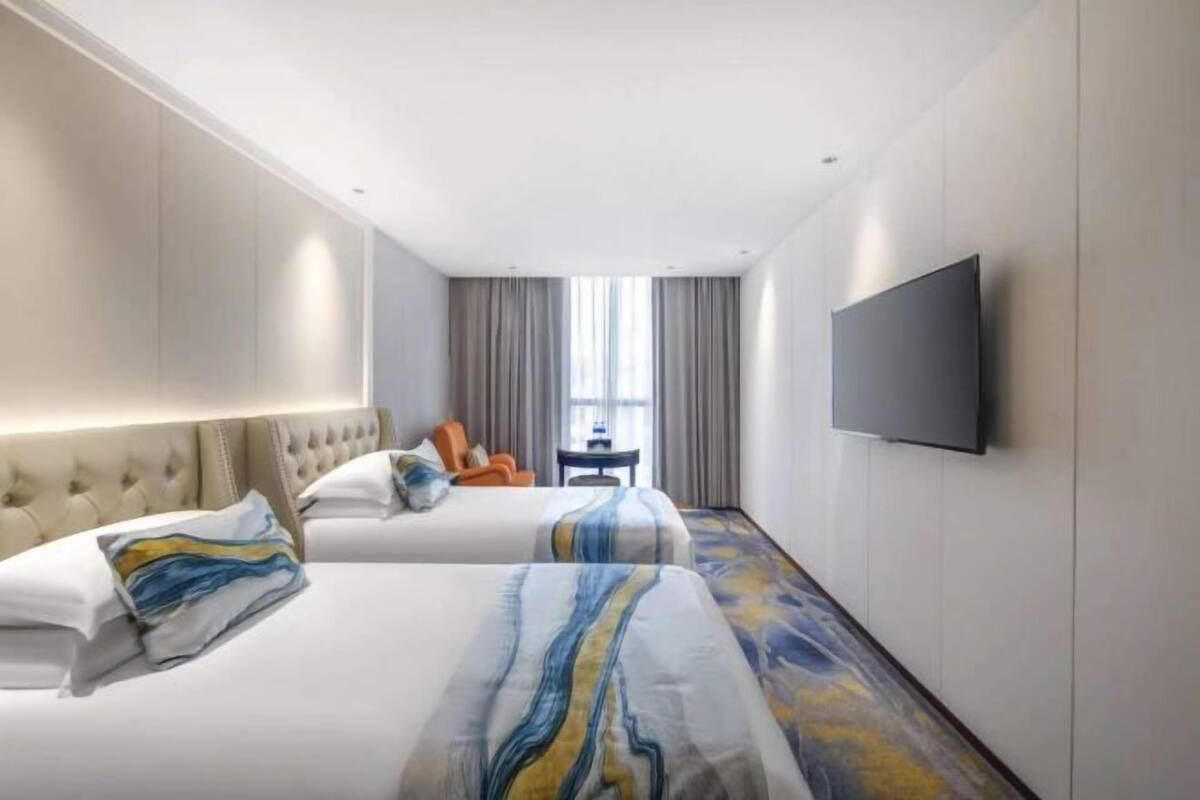 Een hotelkamer met twee bedden, een flatscreen televisie, een raam met gordijnen en een kleine tafel.