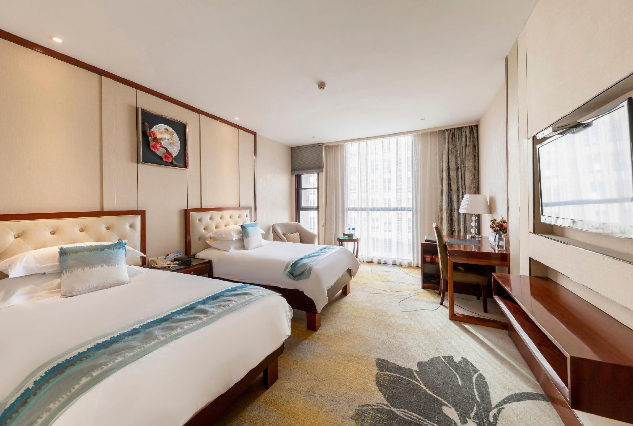 Quarto de hotel com duas camas, uma escrivaninha, uma cadeira, televisão e uma janela grande com cortinas.