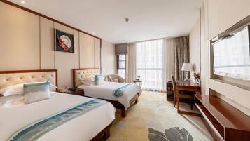 A hotel room with two beds, a desk, a chair, a TV, and a large window with curtains.