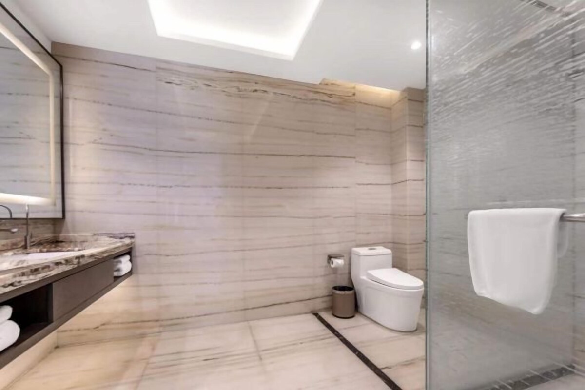 A modern bathroom with a marble countertop, a glass shower enclosure, and a large mirror.