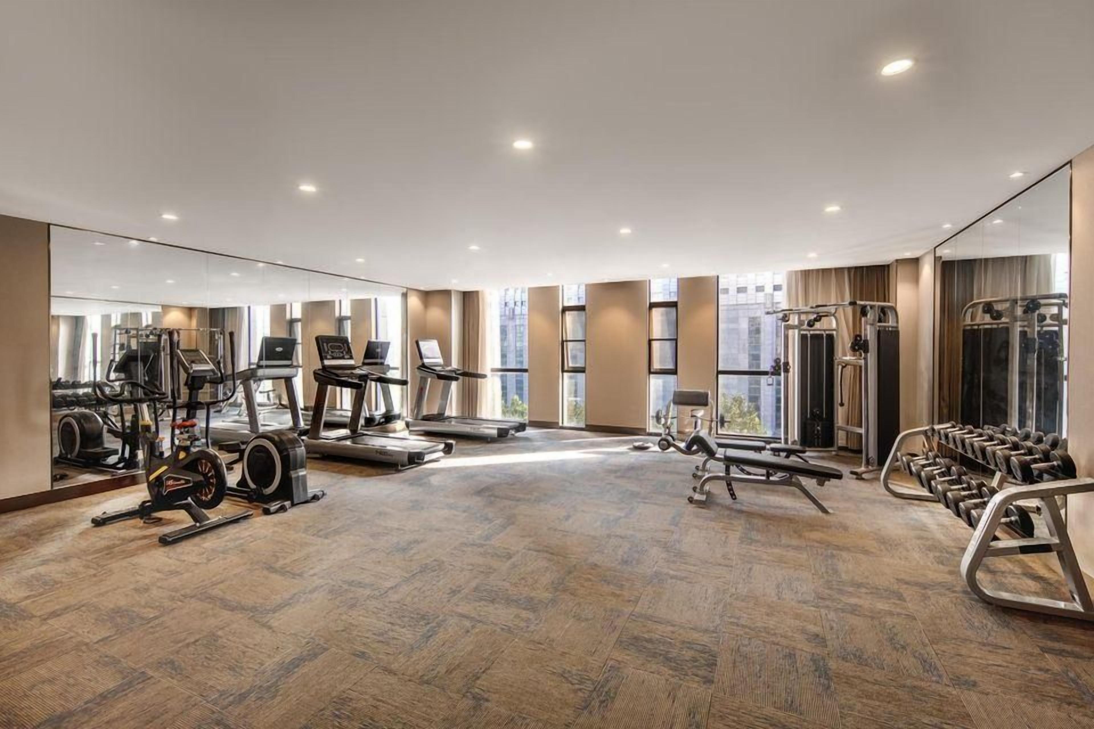 A spacious gym with cardio machines, weightlifting equipment, and a mirrored wall.