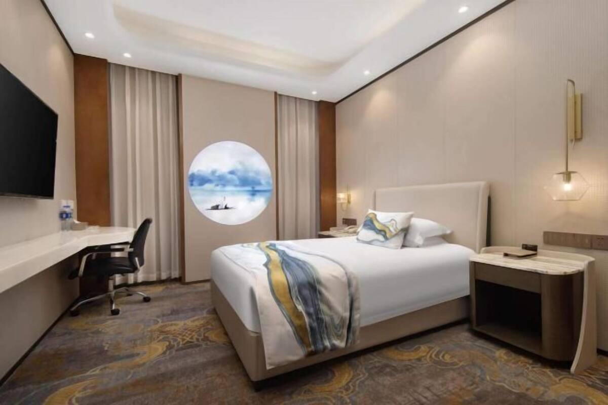 Een hotelkamer met een bed, een bureau, een stoel, een nachtkastje en een aan de muur bevestigde televisie.