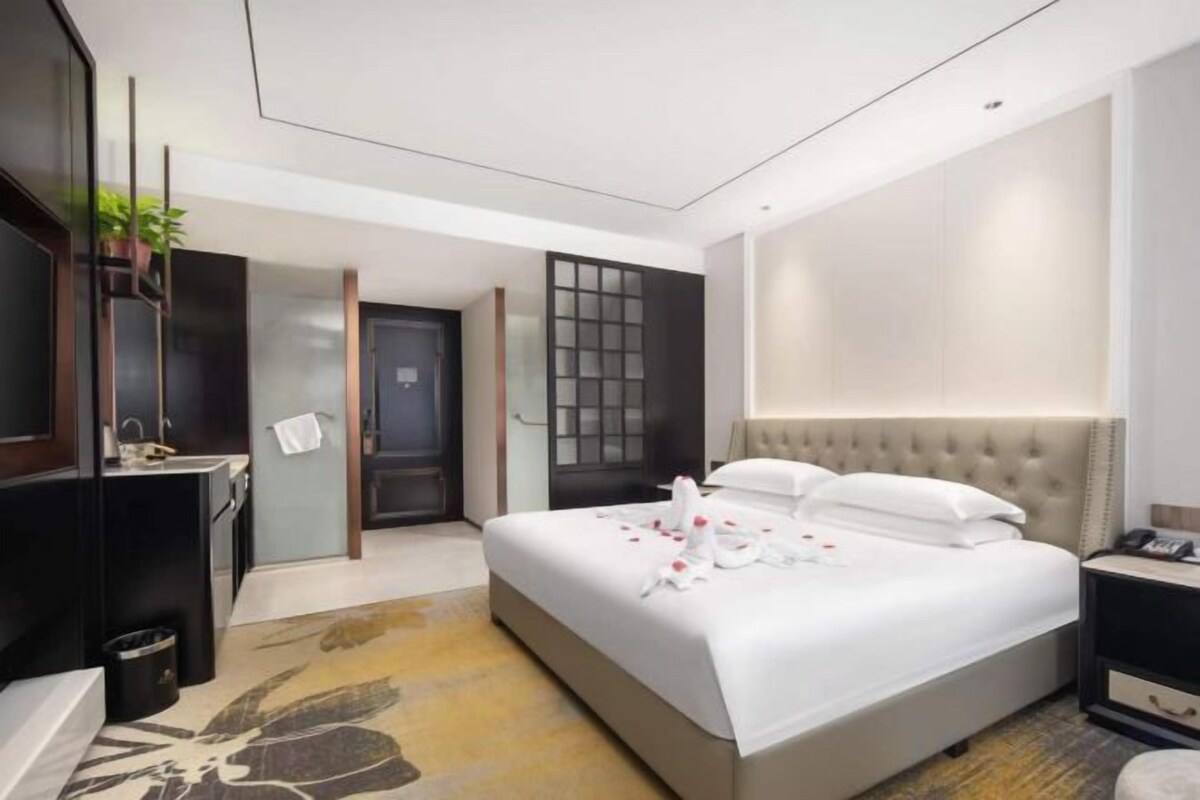 A hotel room with a bed, bedside table, and a mirror.