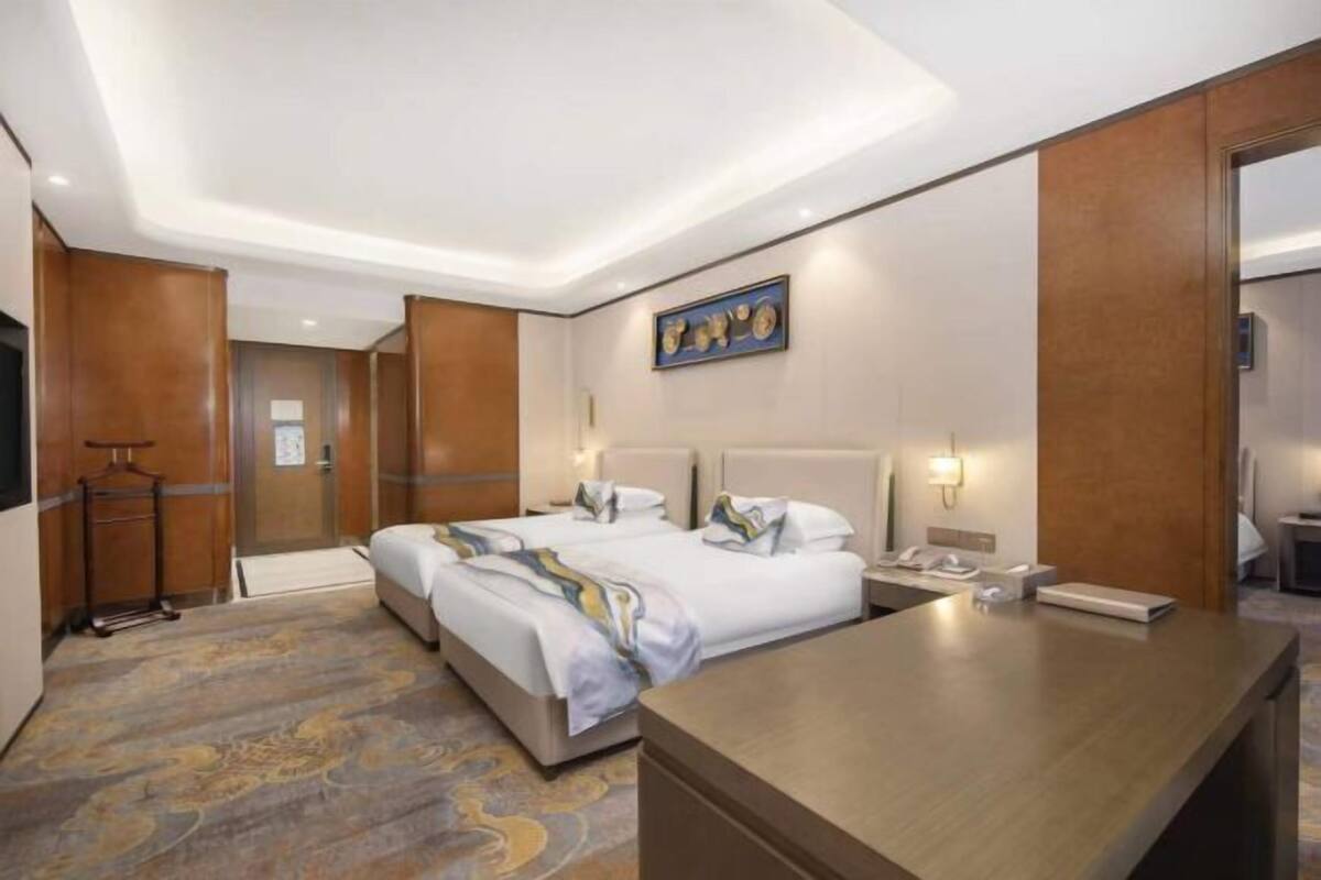 Een hotelkamer met twee bedden, een bureau, een telefoon en een kunstwerk aan de muur.