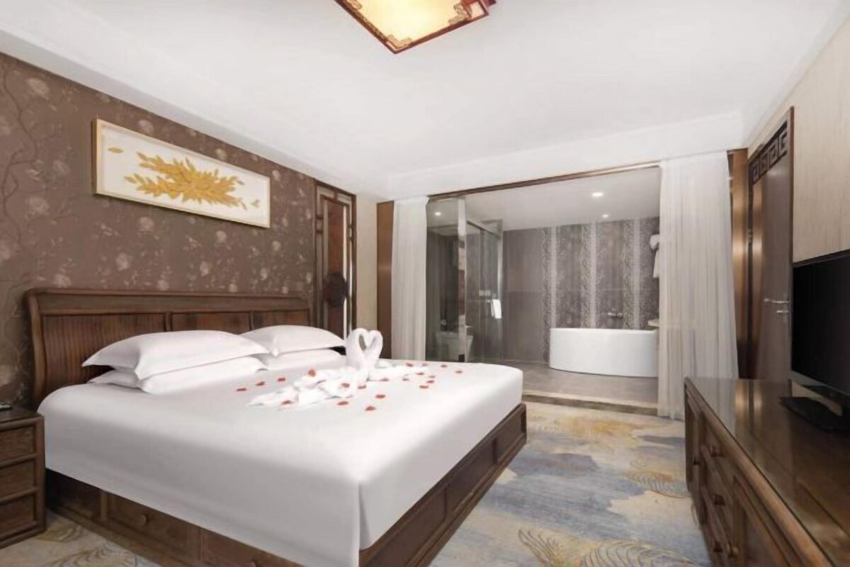 A hotel room with a bed, a television, a bathroom with a bathtub, and a shower.
