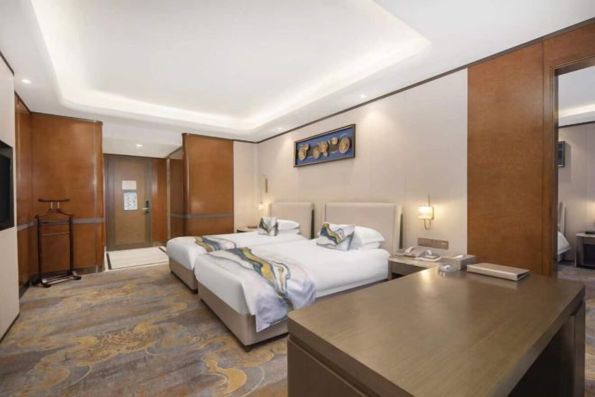 A hotel room with two beds, a desk, a telephone, and a wall-mounted artwork.