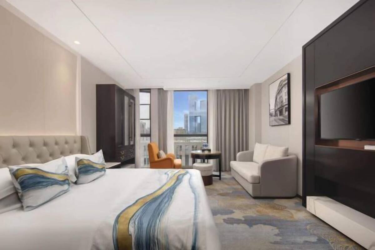 Een hotelkamer met een groot bed, een bank, een televisie en uitzicht op een stadslandschap.