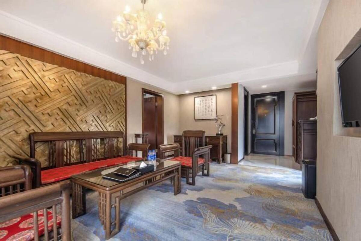 Een hotelkamer met een traditionele houten zithoek, een tafeltje met een laptop, en een kroonluchter.