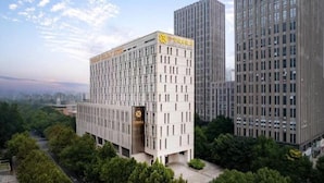 A modern hotel building with a prominent sign, surrounded by other high-rise buildings and lush greenery. - Zhenbao Holiday Hotel (Nanjing Olympic Sports Center) (Nanjing)