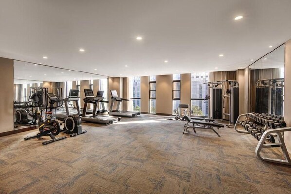 A spacious gym with cardio machines, weightlifting equipment, and a mirrored wall. - Zhenbao Holiday Hotel (Nanjing Olympic Sports Center) (Nanjing)
