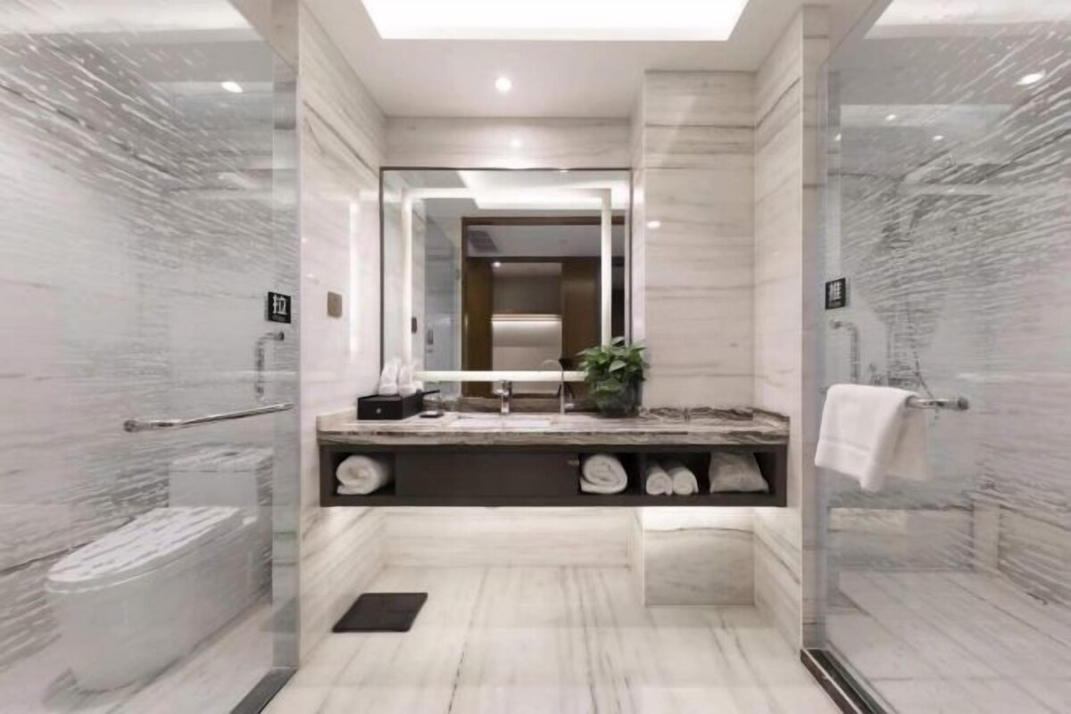 A modern bathroom with a glass shower enclosure, marble walls, and a built-in vanity with a mirror.