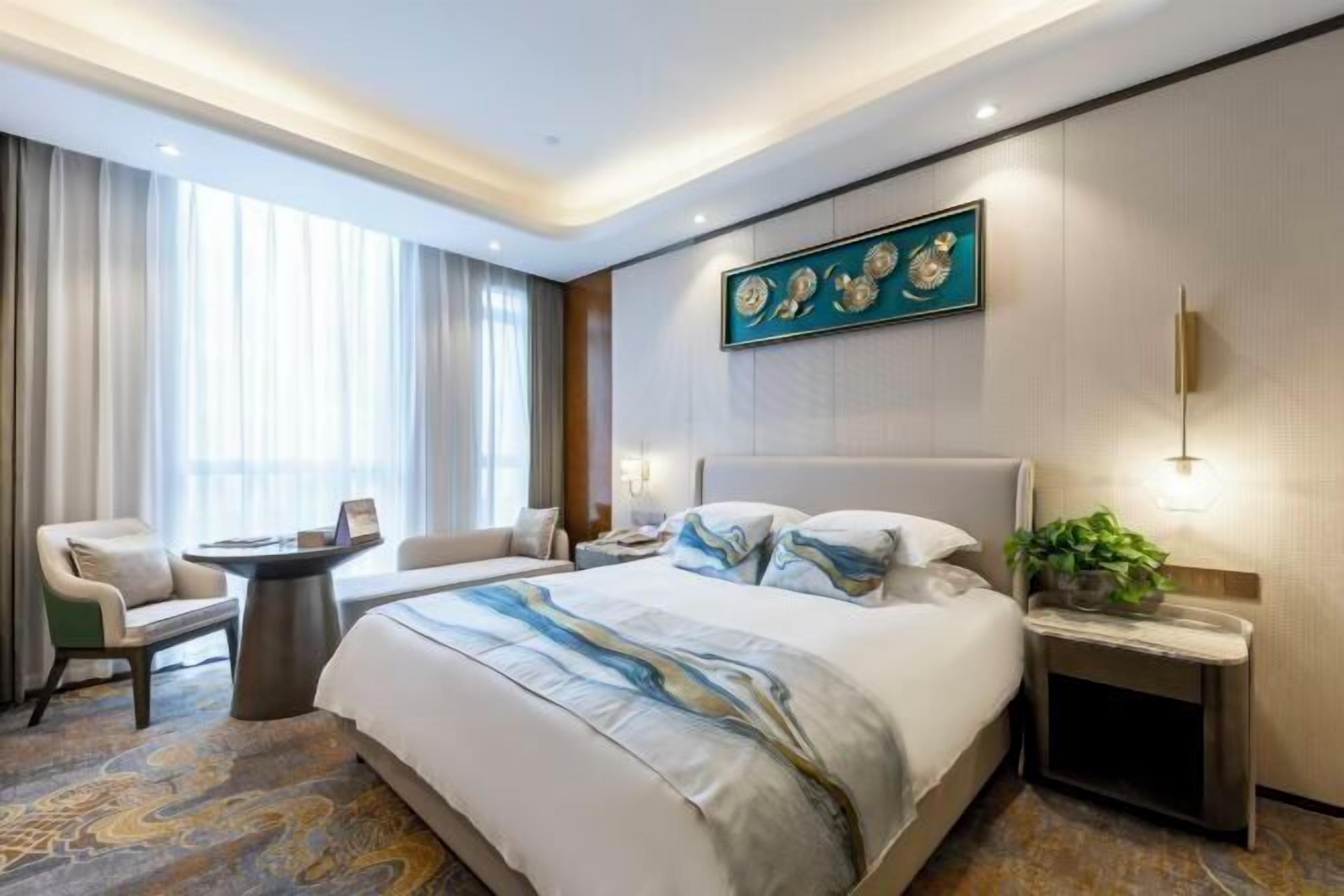 A hotel room with a large bed, a bedside table, a chair, a desk, and a window with curtains.